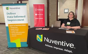 Rpresenmtative for Nuventive sitting at sponsorship table with Nuventive branded table cover