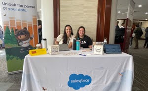 2 Salesforce representatives sitting at Salesforce sponsorship table wioth branded table cover